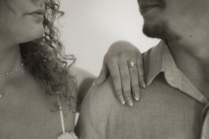 Sepia-toned detail shot of engagement ring and couple's tender moment.
