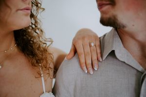 Close-up shot highlighting engagement ring as woman rests hand on partner's shoulder.