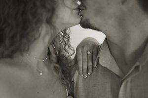 Intimate black and white portrait of a couple in a tender moment with curly hair and hands touching.