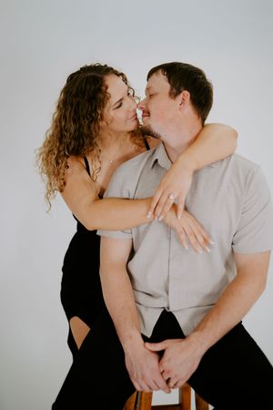 An intimate portrait of a couple sharing a tender moment while seated on a wooden stool.