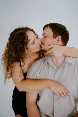 A couple shares a passionate embrace during an intimate photoshoot against a white backdrop.