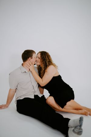 Intimate couple lying together on white background in casual attire showing affection.