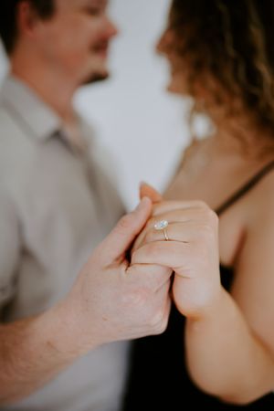 Close-up shot of hands holding with an engagement ring visible against a blurred background.