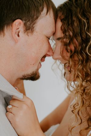 A close-up portrait captures a tender moment between a couple against a light background.