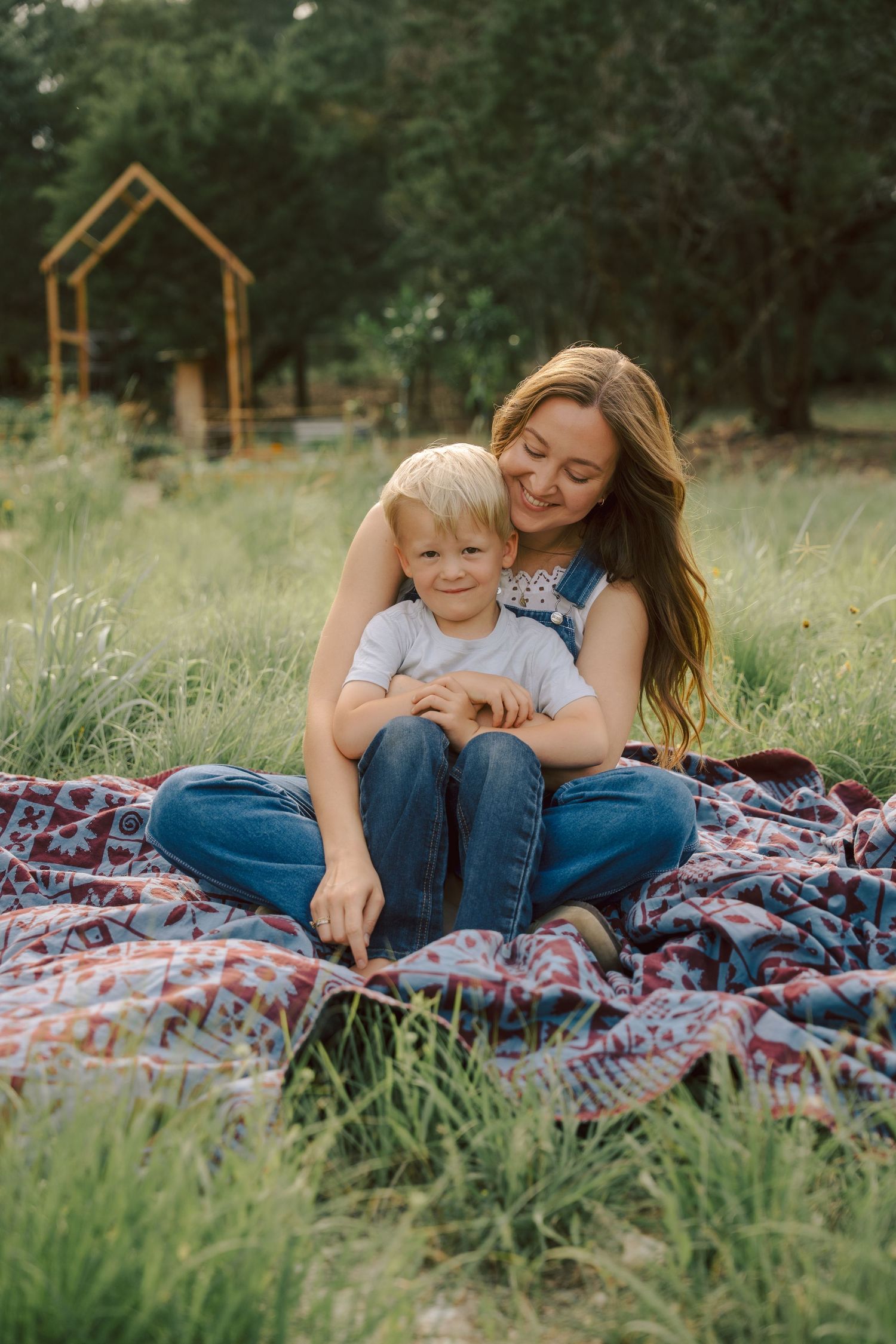 A loving moment shared on a colorful blanket in a grassy field with a wooden playhouse structure in the background.