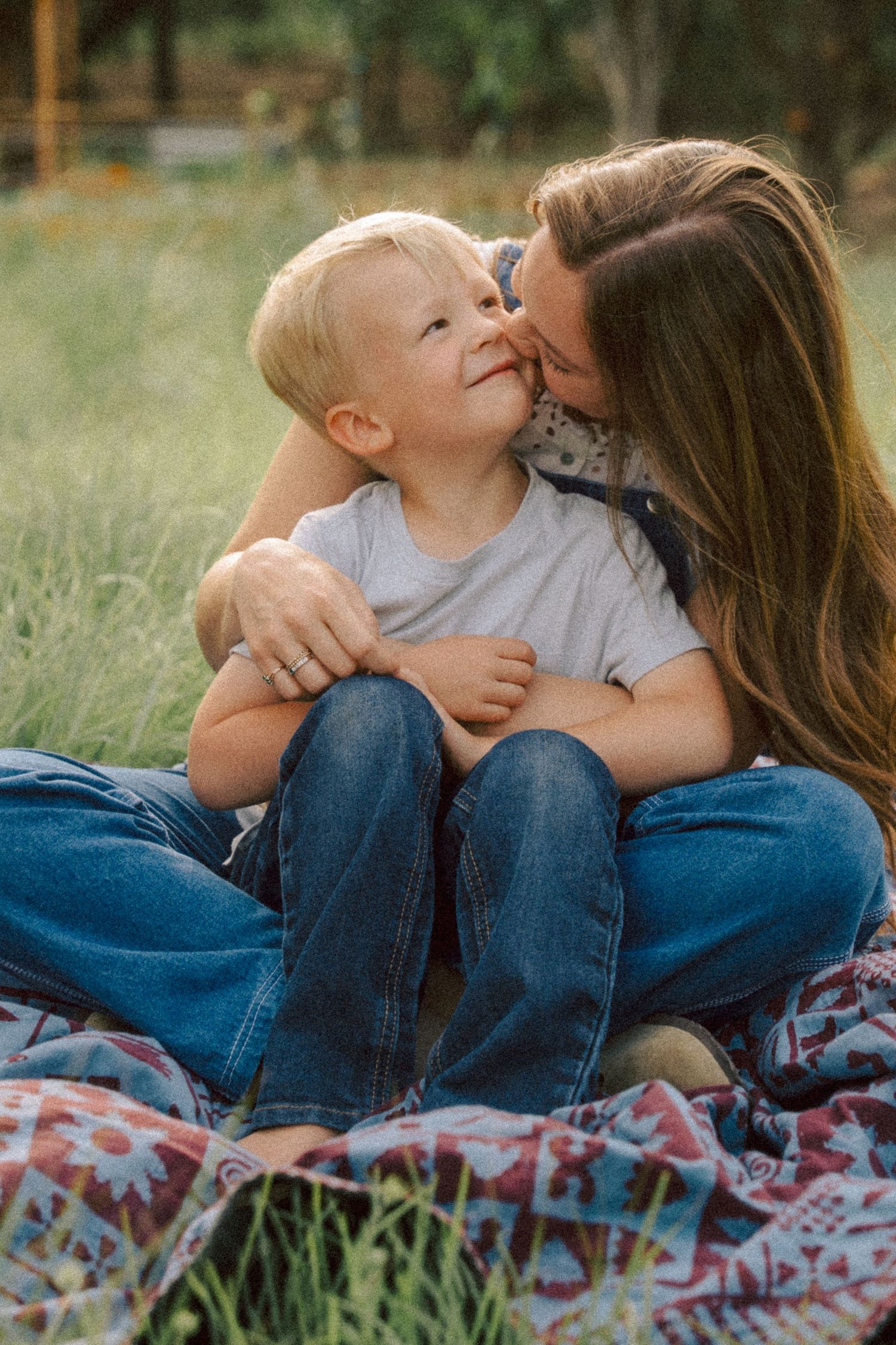 A tender moment captured on a picnic blanket in tall grass as parent and child share affection and laughter.