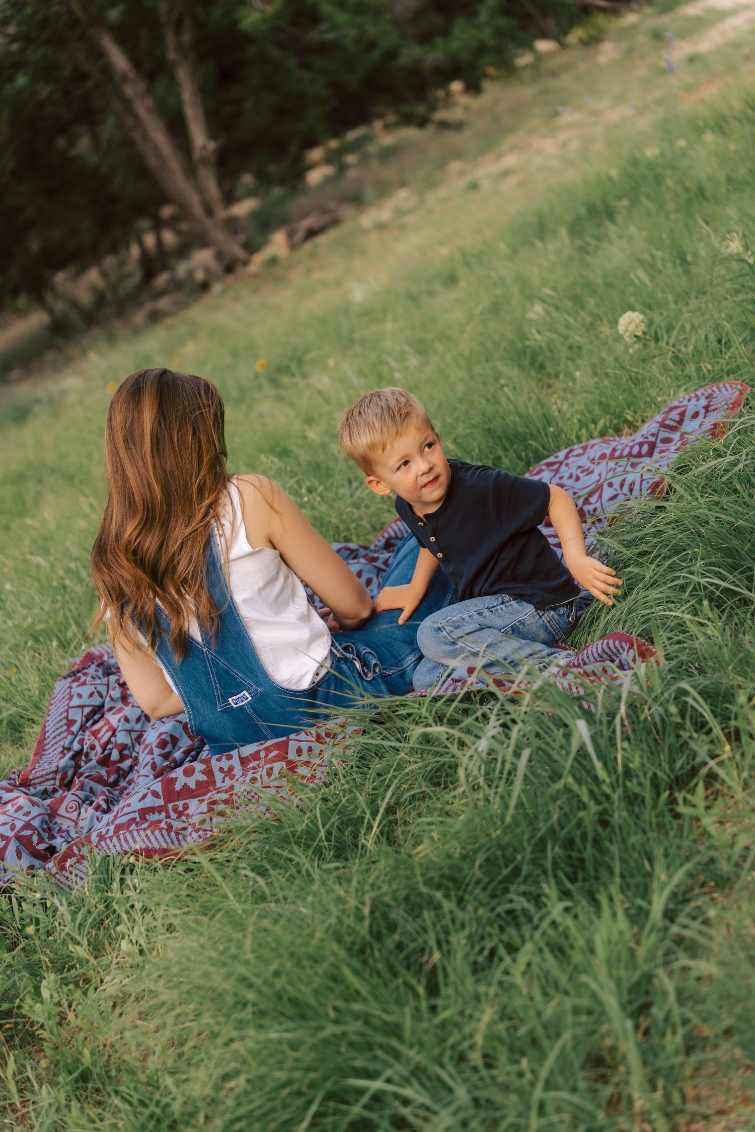 Two people relaxing on a colorful blanket spread across a grassy hillside on a sunny summer day.