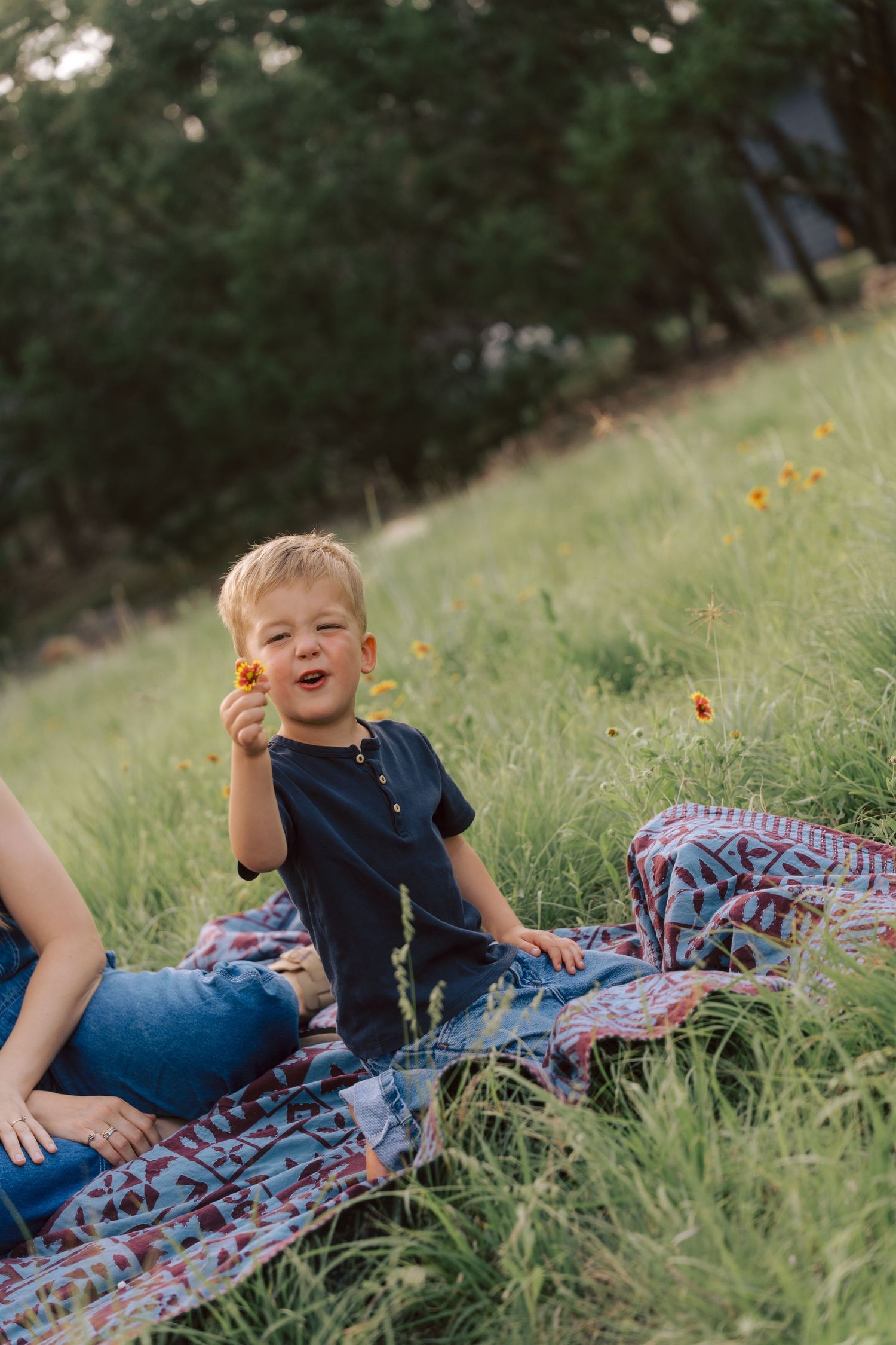 A child sits on a patterned blanket in a grassy field with wildflowers during golden hour.