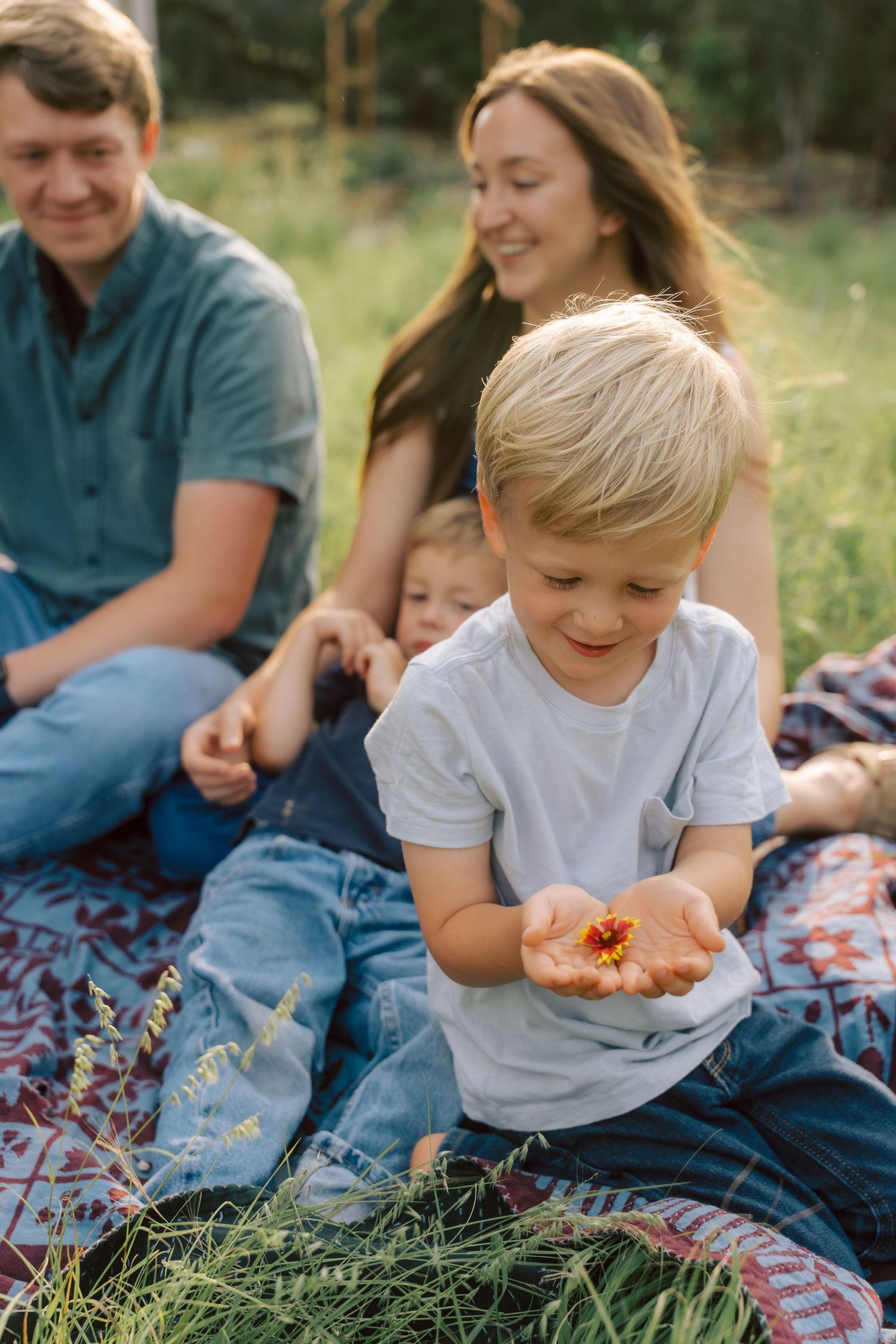 Family picnic scene showing casual moments together as they sit on a blanket outdoors.