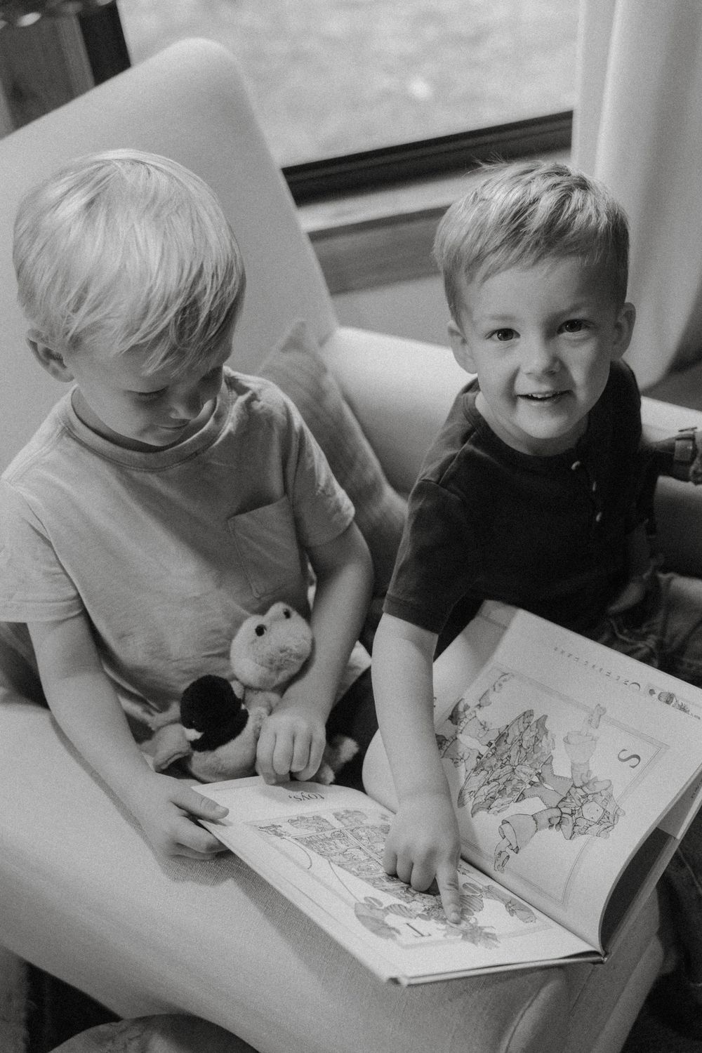 Two young children sitting together reading a picture book in black and white photography.