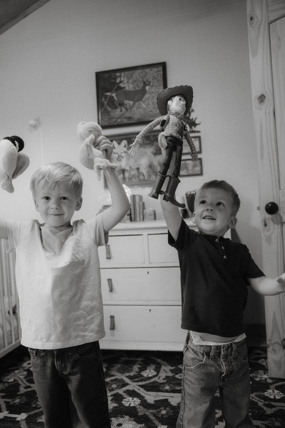 Two children playing with toys and showing excitement while standing in front of a white dresser in black and white.