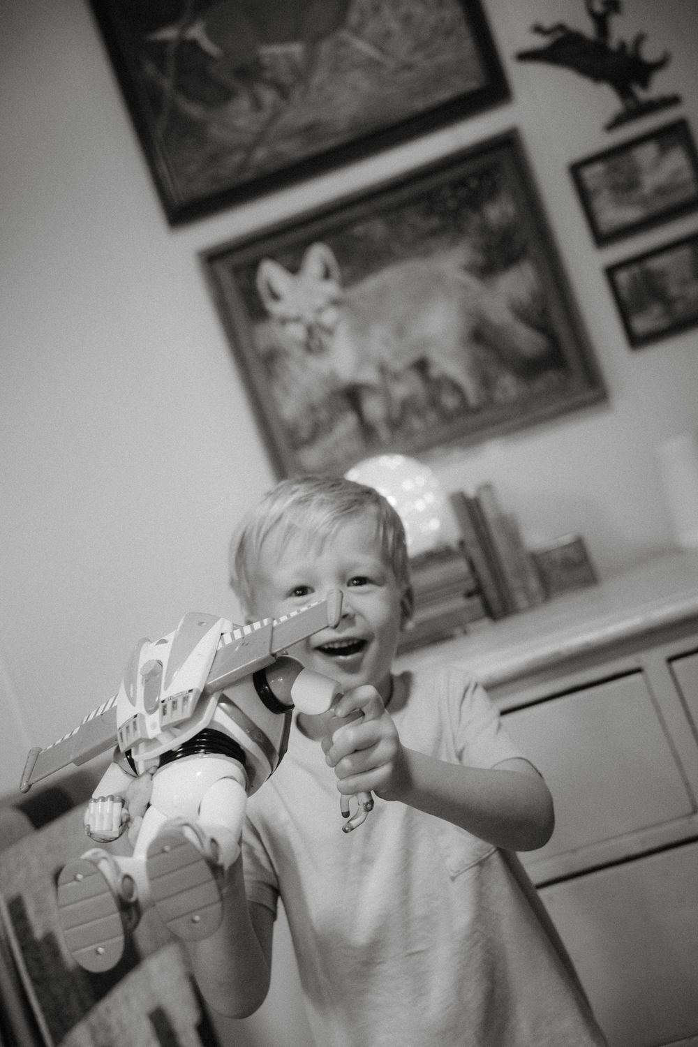 A joyful child plays with a toy dinosaur while standing in a room with wildlife artwork on the walls.