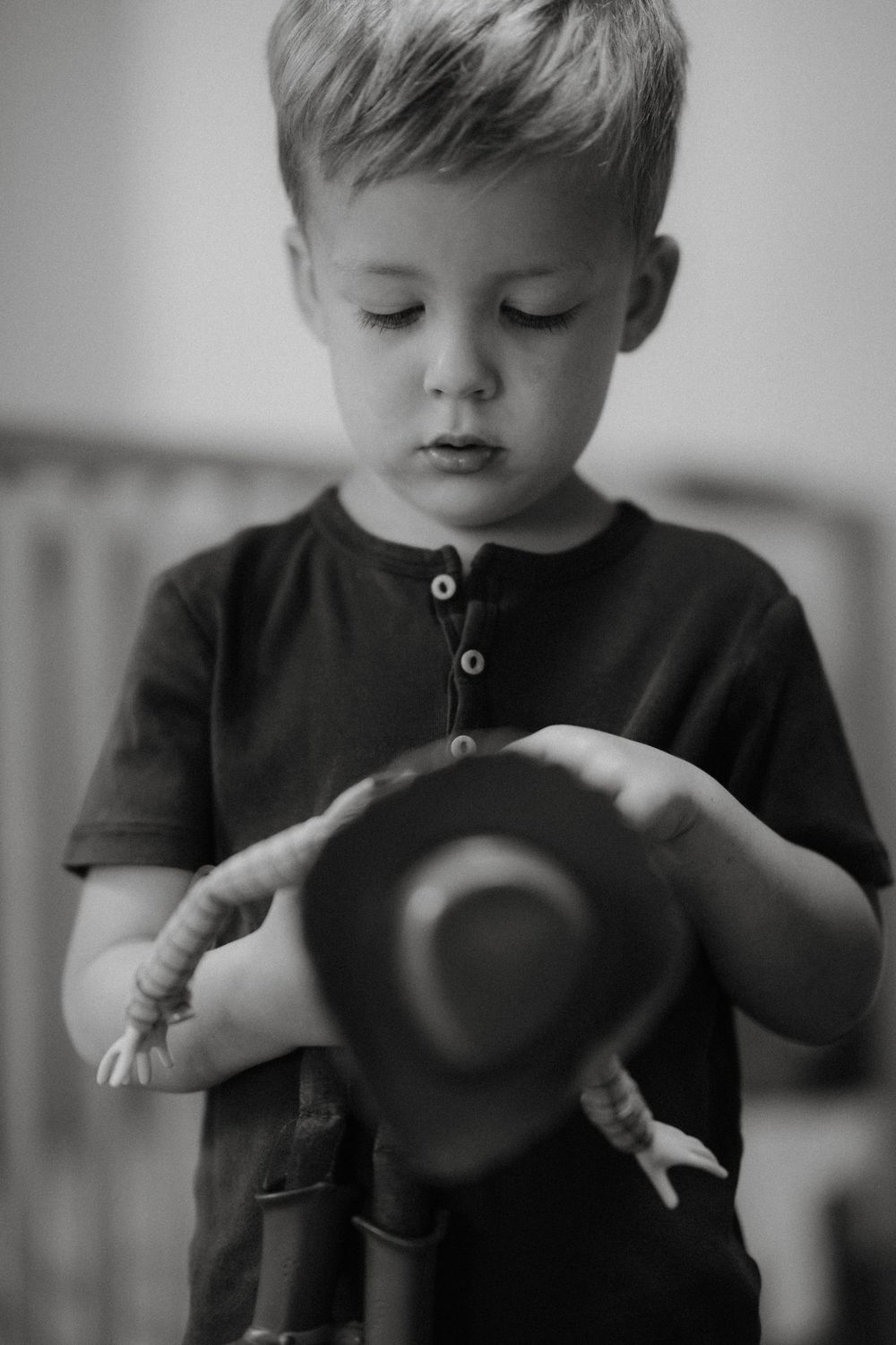 A young child in a dark shirt examines a small hat in their hands in this black and white portrait.