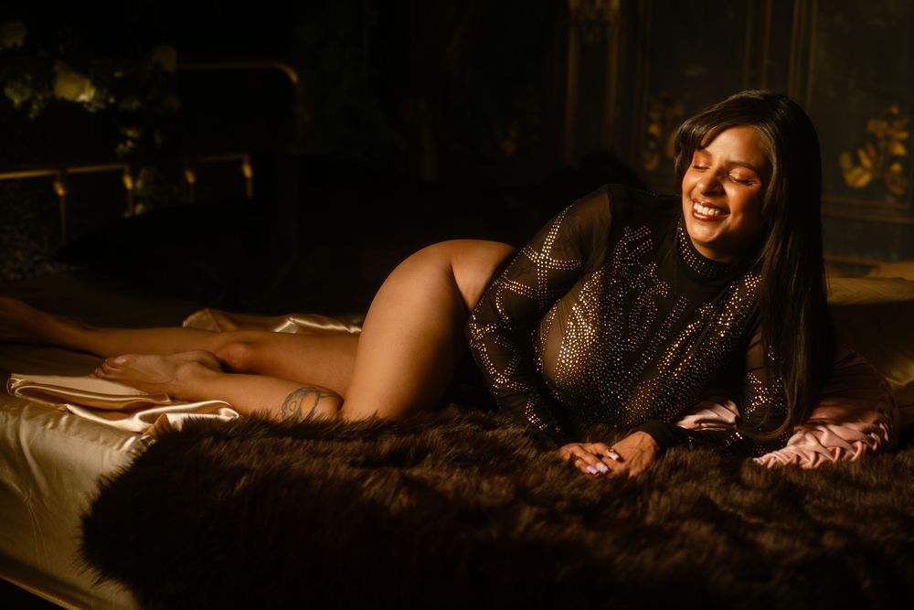 A person poses on a dark fur rug in dim lighting wearing a sparkly long sleeve bodysuit during a boudoir photoshoot in Fort Worth, TX.