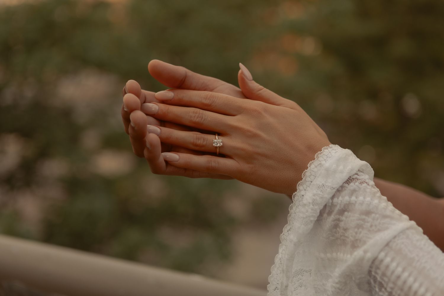 Close-up of hands of a man placing engagement ring on woman's finger during golden hour.