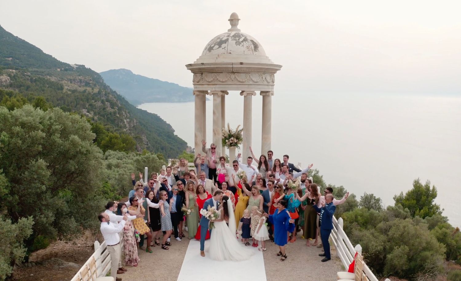 Wedding ceremony at a scenic viewpoint overlooking the sea, surrounded by friends and family.