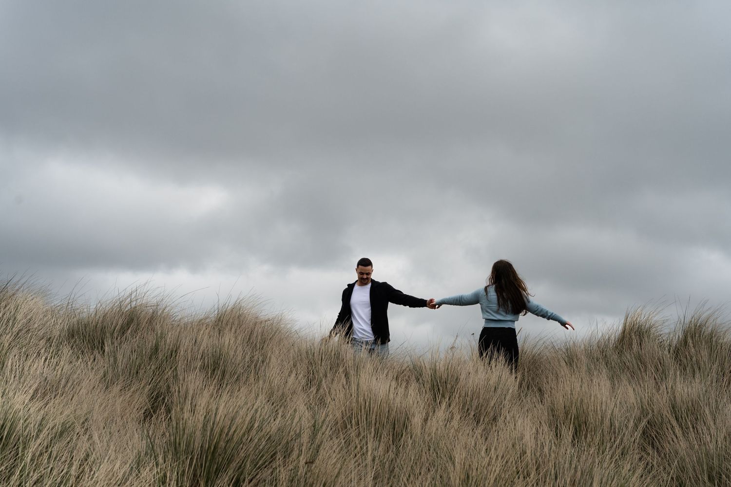 Two figures stand in a mountain meadow filled with white wildflowers at sunset.