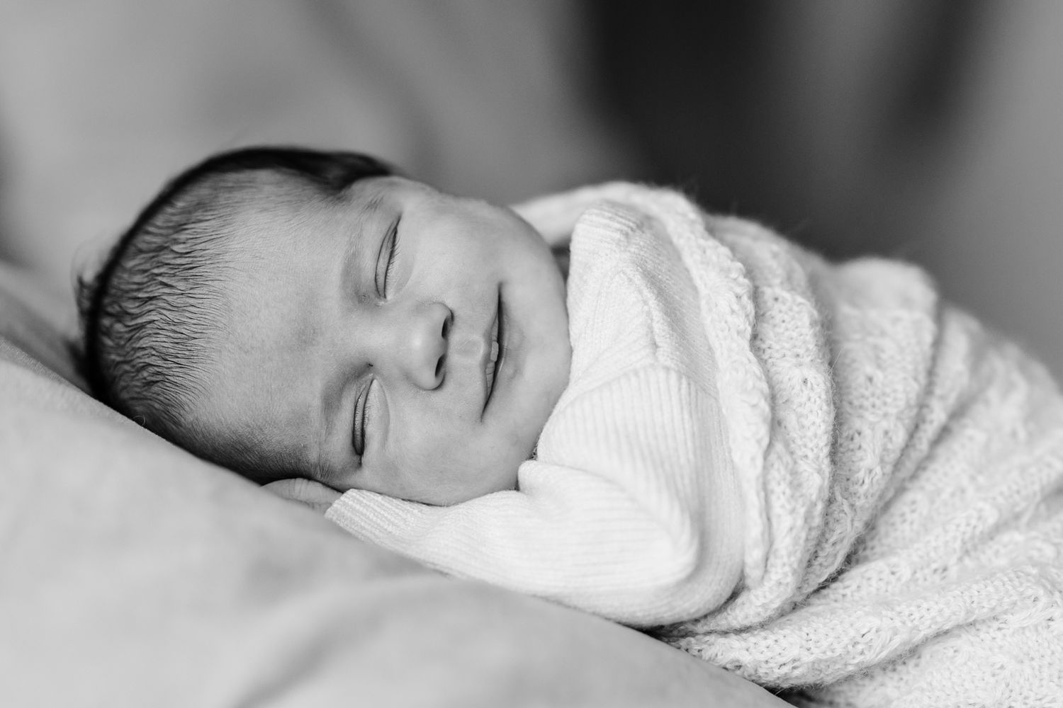 a baby yawning, whilst it's head is cradled in its mother's hands