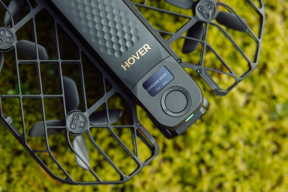 Close-up detail of a Hover 2 drone propeller guard and camera system against a blurred green background.