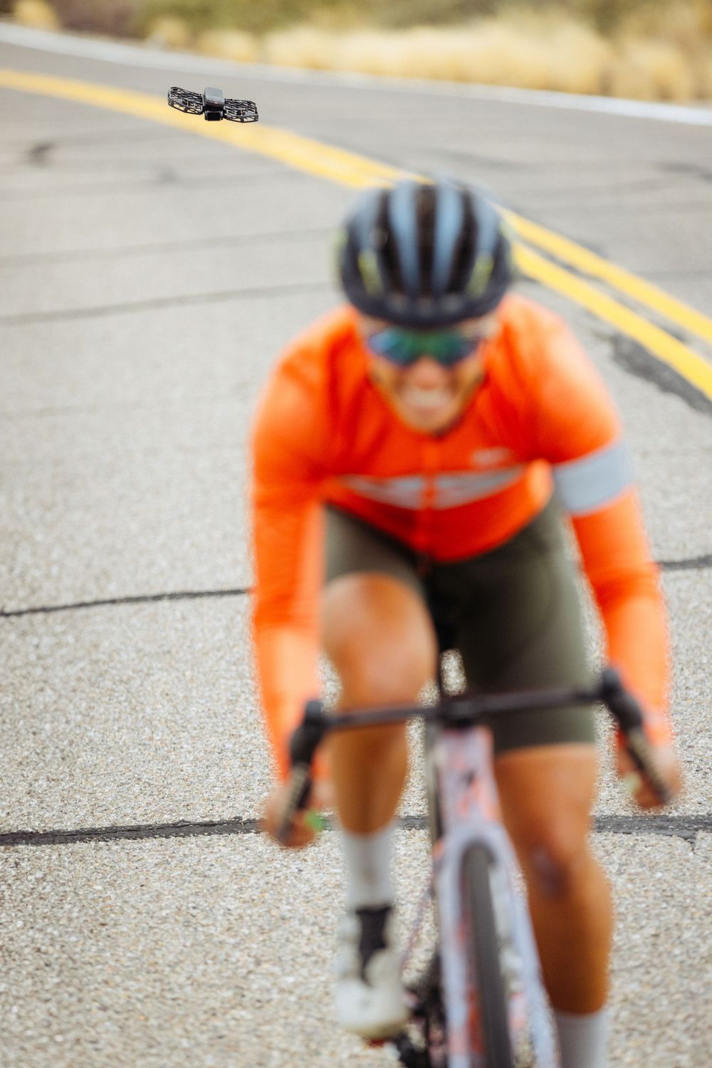 Close-up of a cyclist in bright orange jersey on a road bike leaning forward in an aerodynamic racing position.