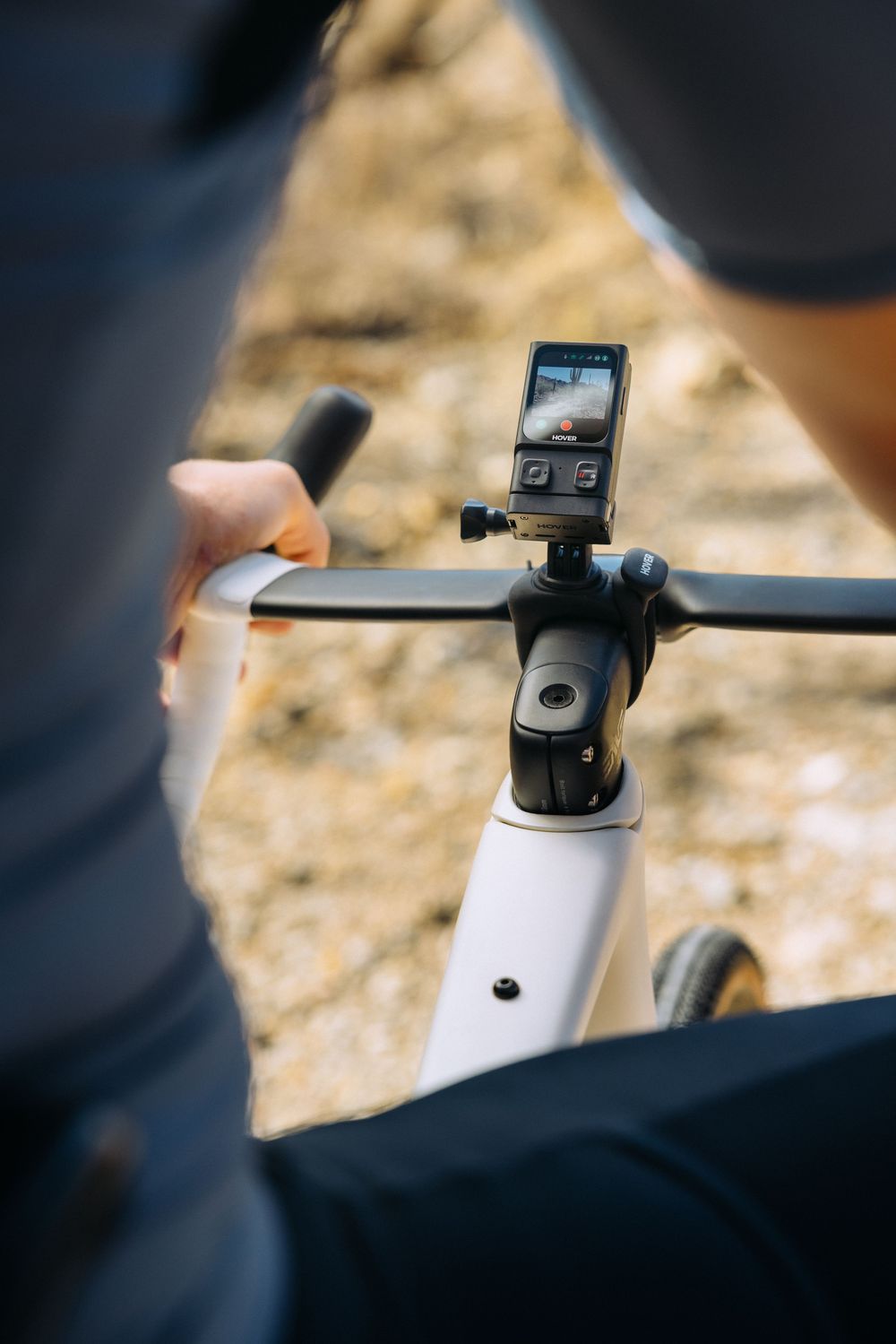 A bicycle handlebar mounted with a small digital device or bike computer against a blurred beige background.