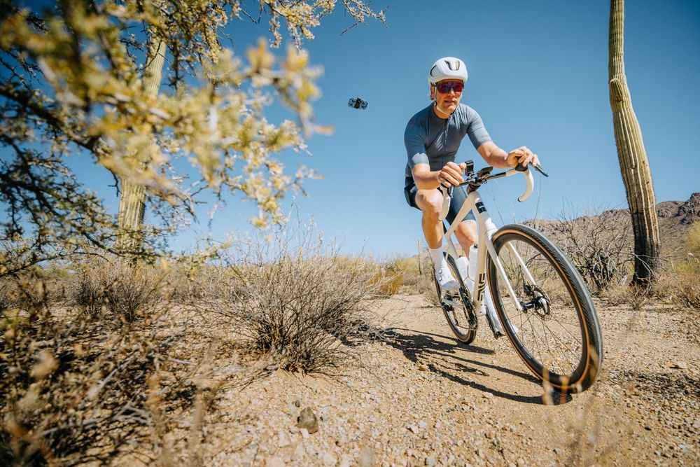 Mountain biker rides along desert trail with saguaro cactus and desert vegetation against blue sky backdrop.