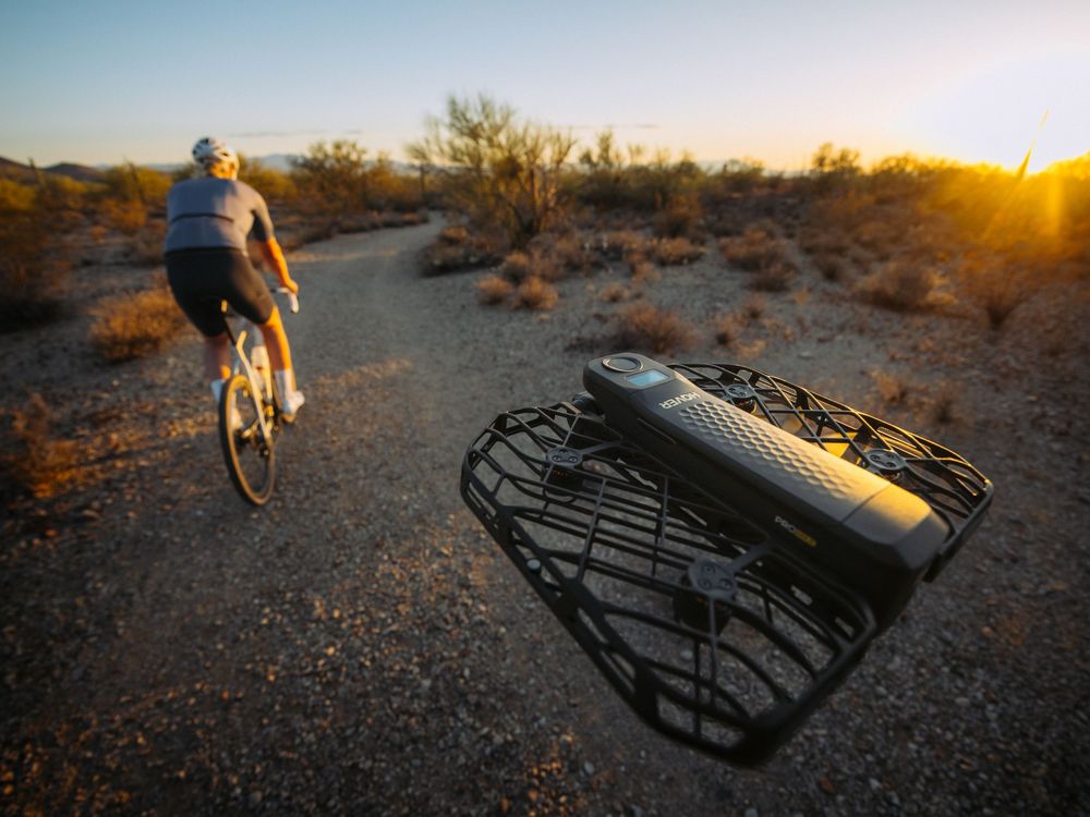 A cyclist rides into the desert sunset with a bike rack or equipment visible in the foreground.