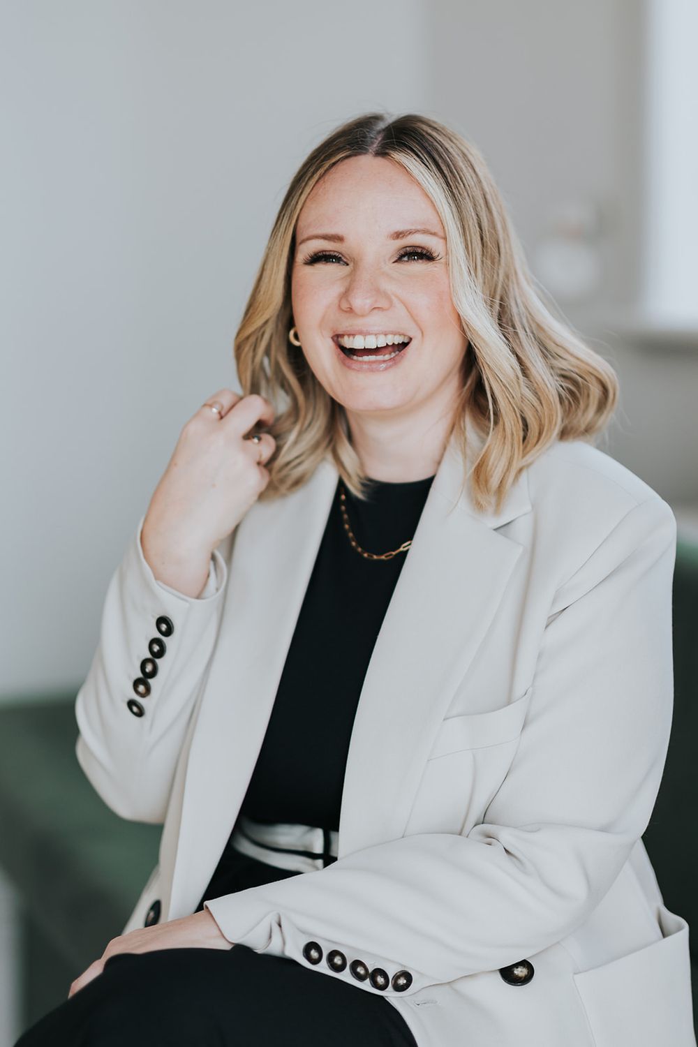 Professional portrait of someone in a white blazer and black top laughing joyfully against a light background.