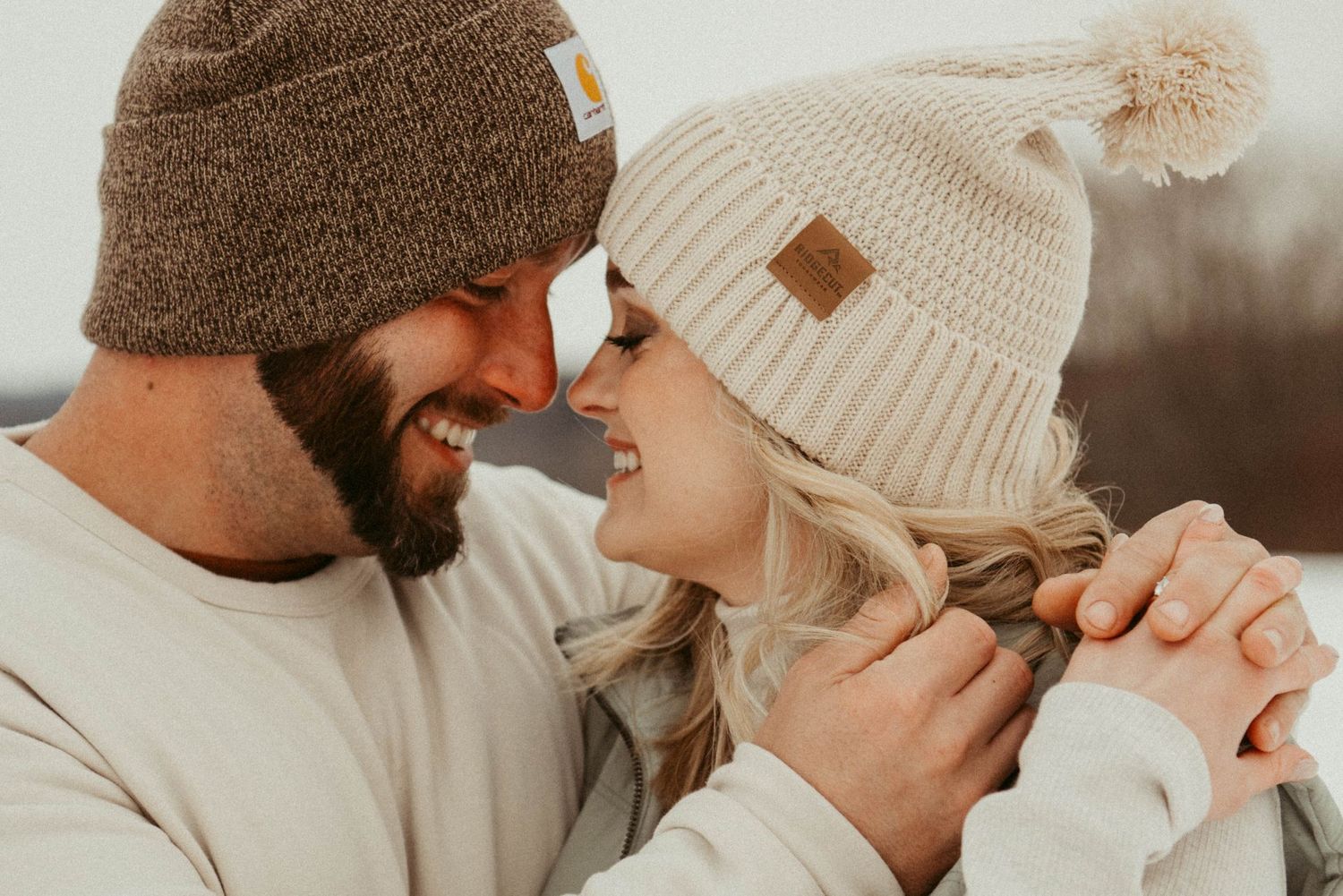 Couple in knit beanies laughing together while holding warm beverages.