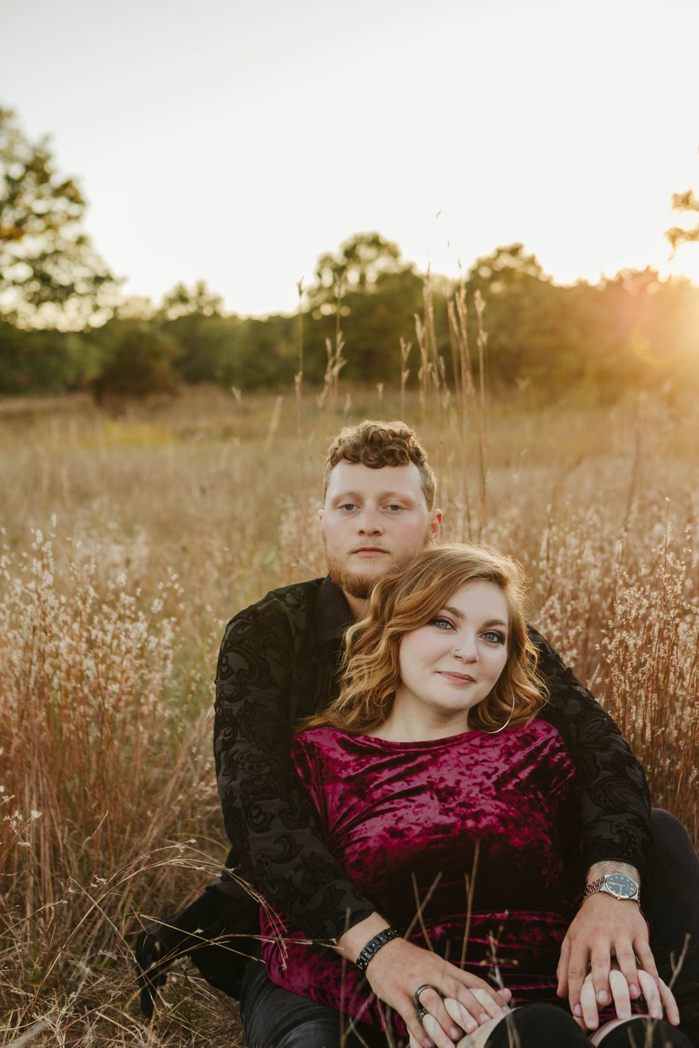 Couple in casual attire pose together in a sun-lit field of tall grass.