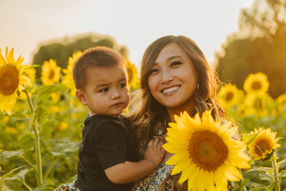 Mother and child standing in sunflower field at golden hour.