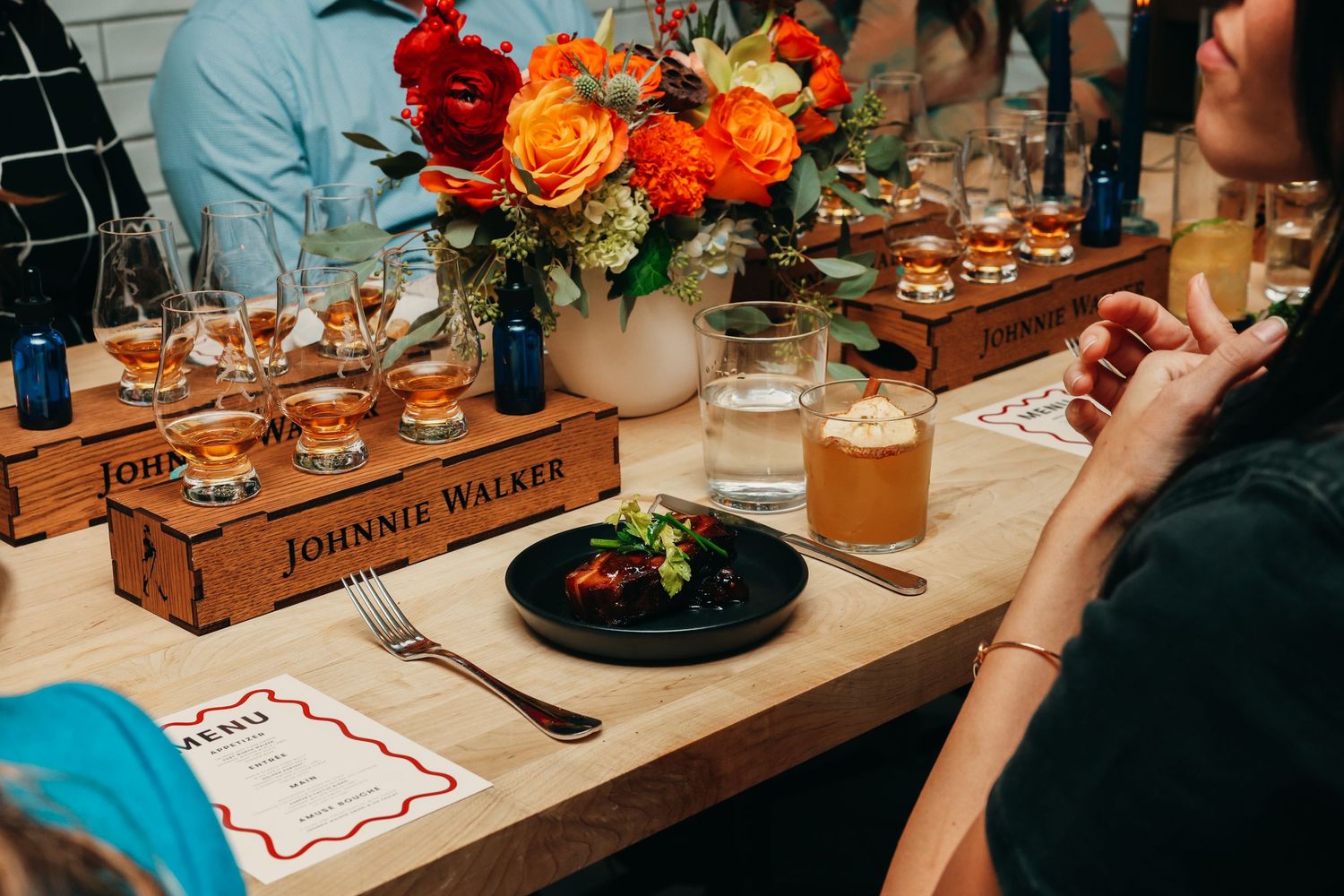 Elegant table setting with orange floral centerpiece and bourbon flight tasting arrangement.