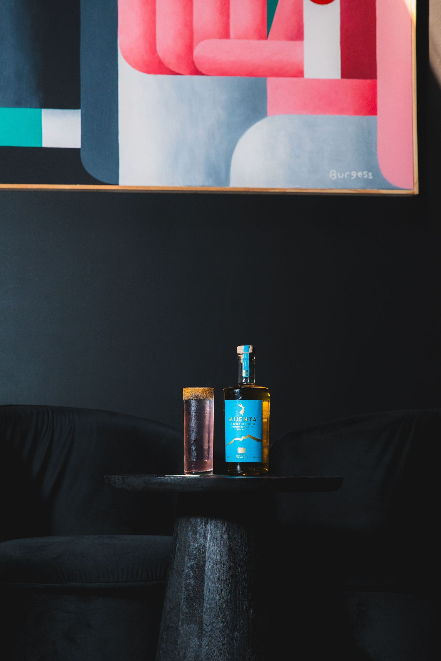 Minimalist bar setup with bottles against geometric pink and blue wall art.