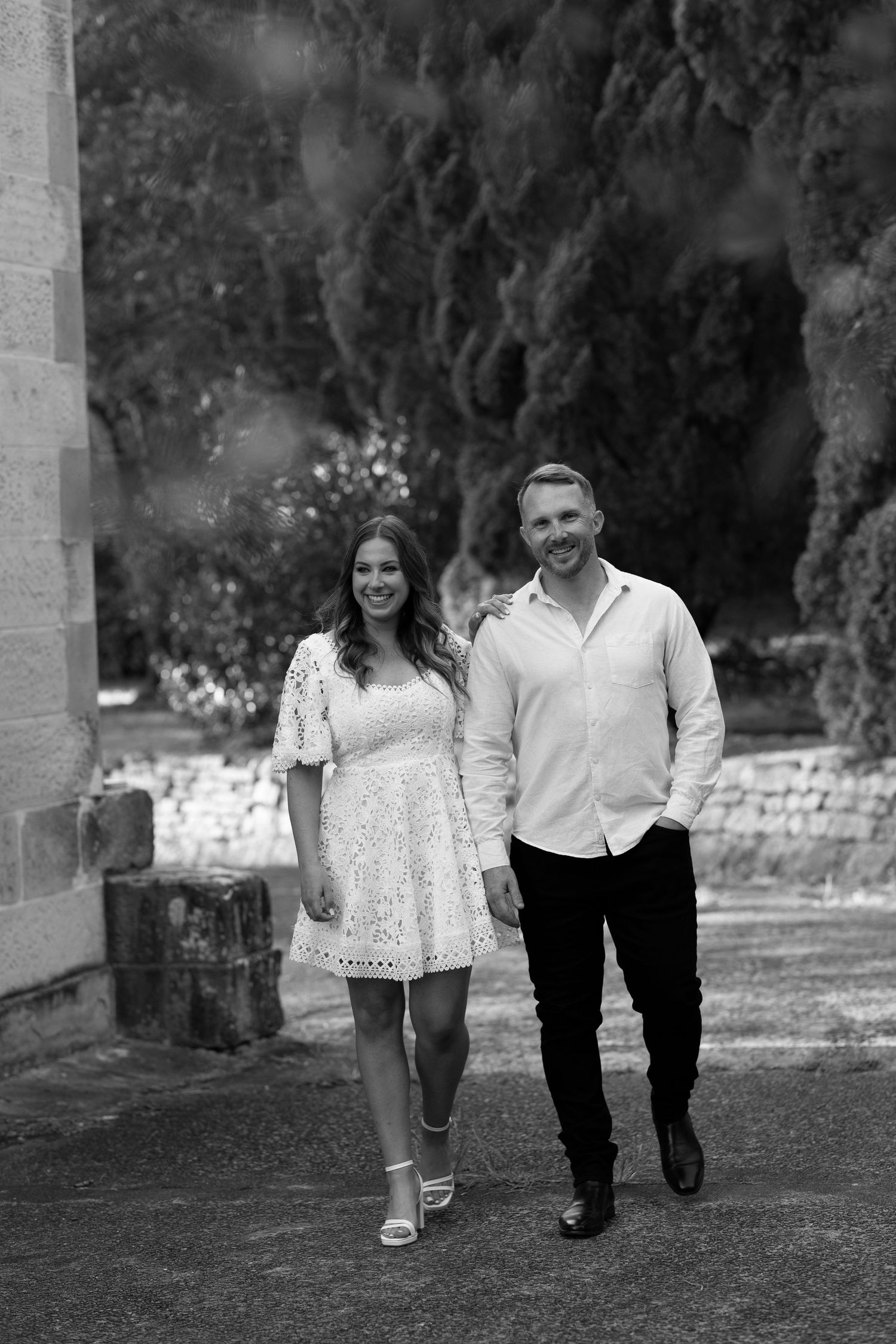 A couple walks playfully through a garden pathway holding hands in a progressive motion sequence in black and white.