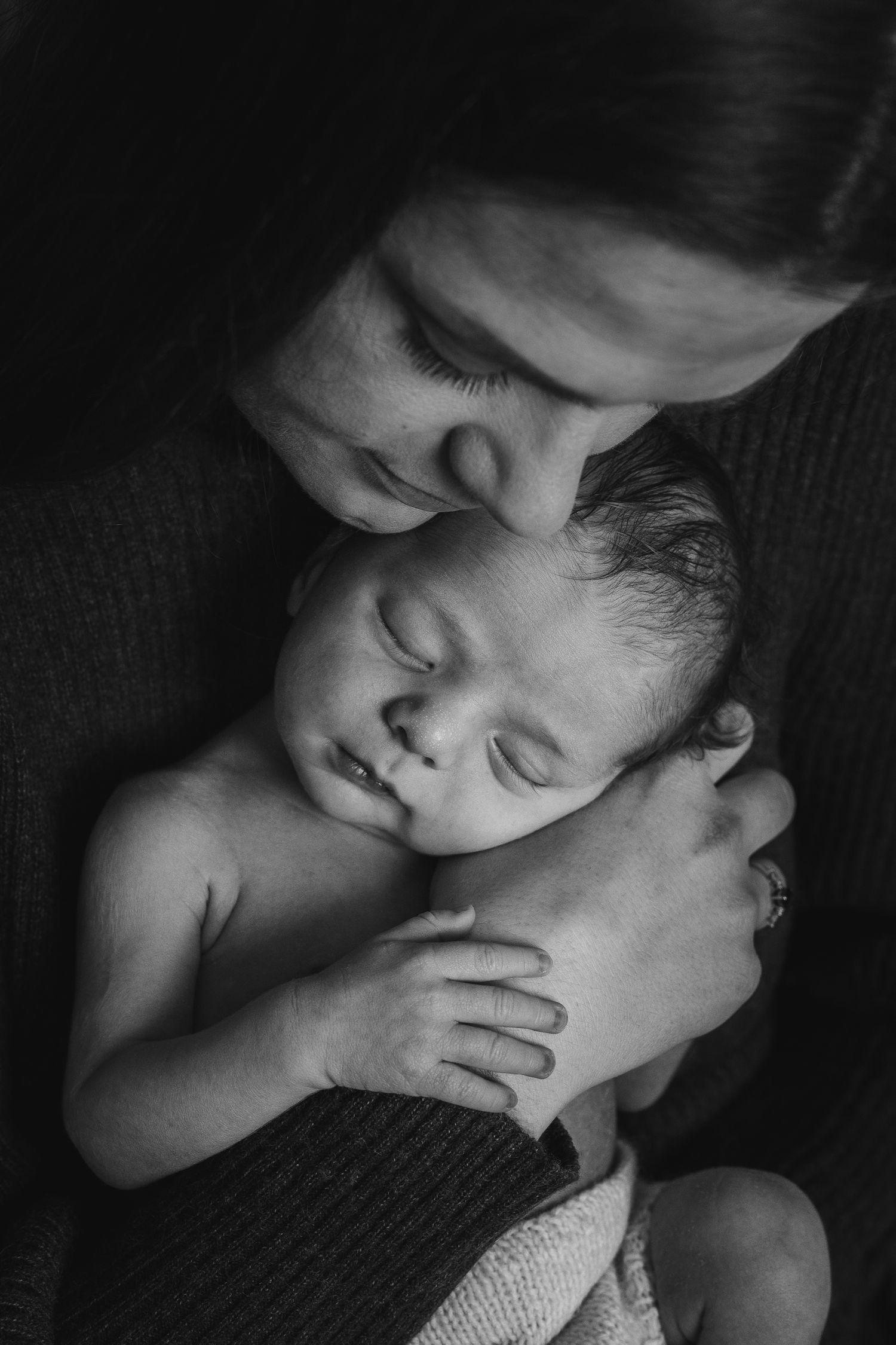 Black and white intimate portrait of a tender embrace between parent and baby displaying nurturing love and connection.