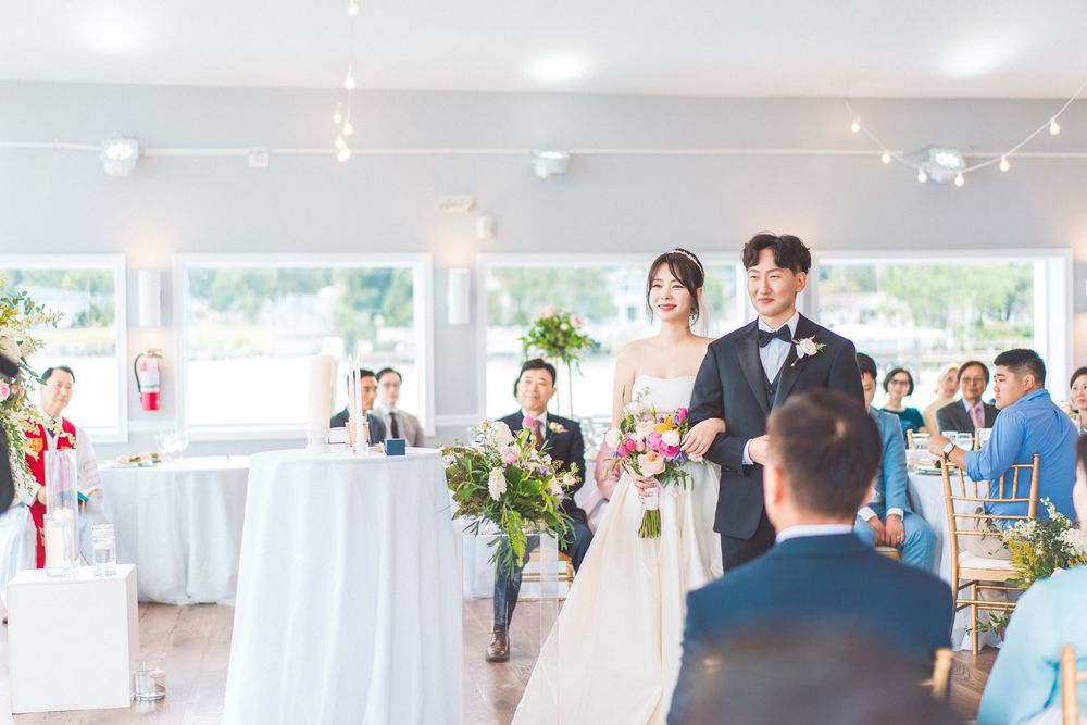 Wedding couple walking down aisle in bright reception venue with guests watching.