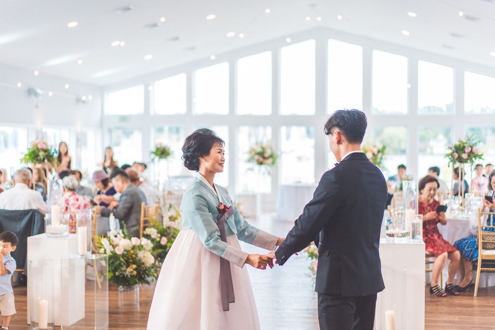 A touching moment during a wedding ceremony in a bright venue with large windows and floral decor.