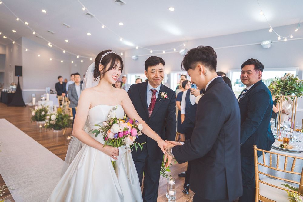 Wedding ceremony participants exchange rings in an elegant venue decorated with floral arrangements and string lights.