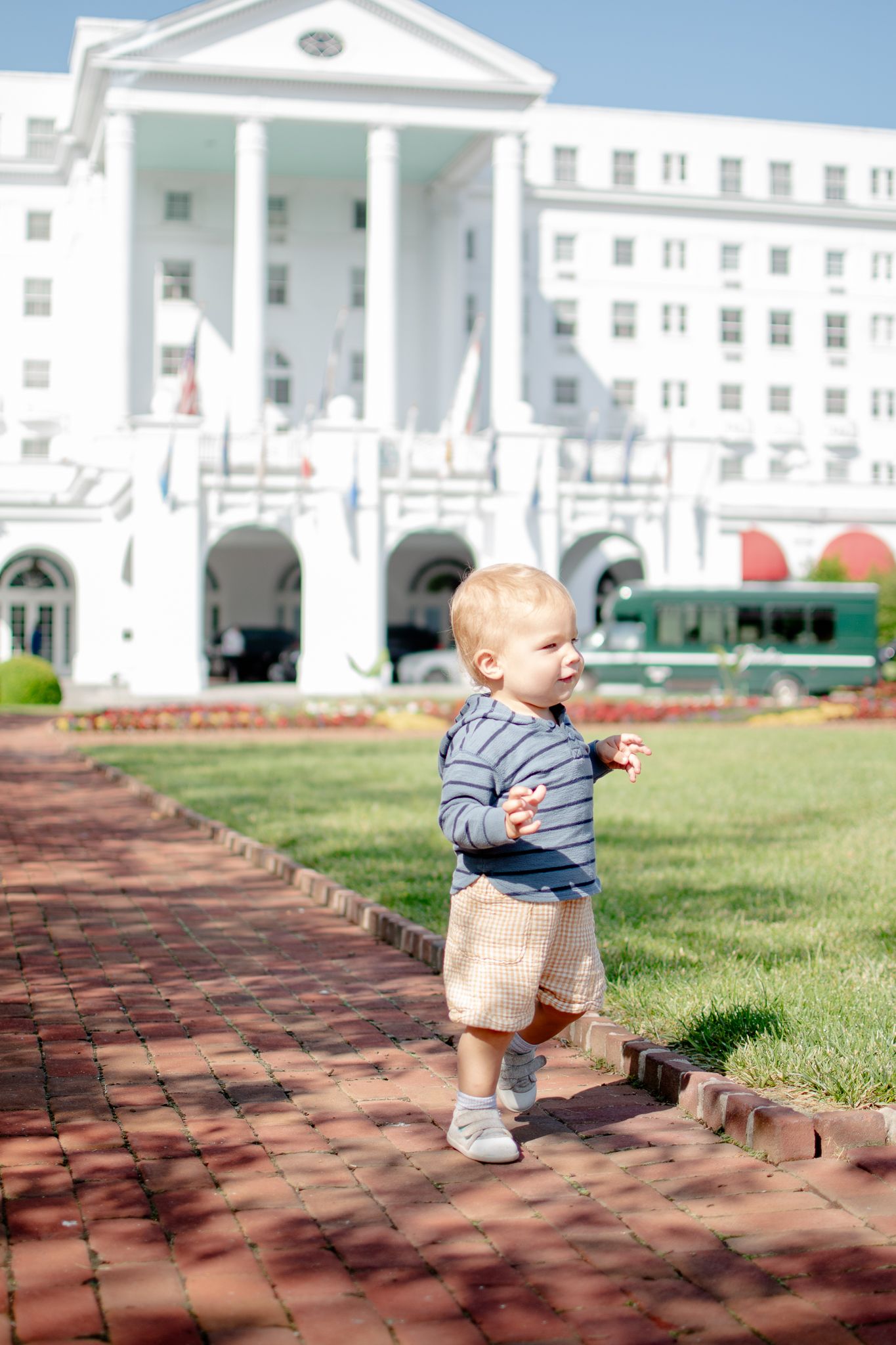 Child walking on brick path in front of grand historic Greenbrier Resort with white columns and arches.