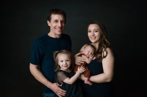 Professional family portrait series in dark and moody lighting showing parents and young child in intimate poses.