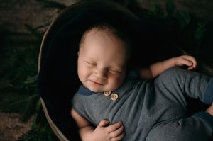 Sleeping baby dressed in gray outfit rests peacefully in wooden basket.