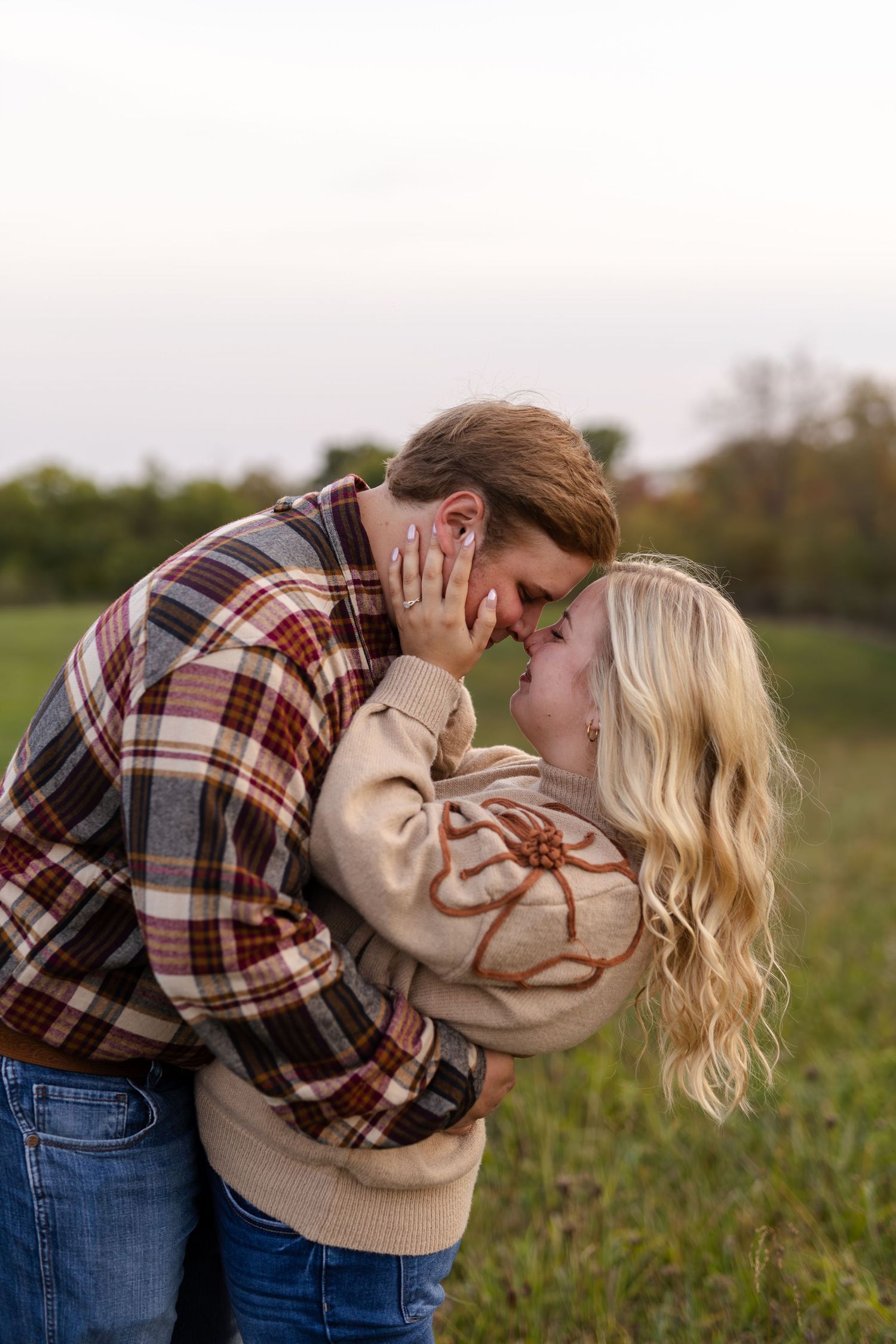 Black and white photo of a couple sharing a romantic kiss in an open field during golden hour.