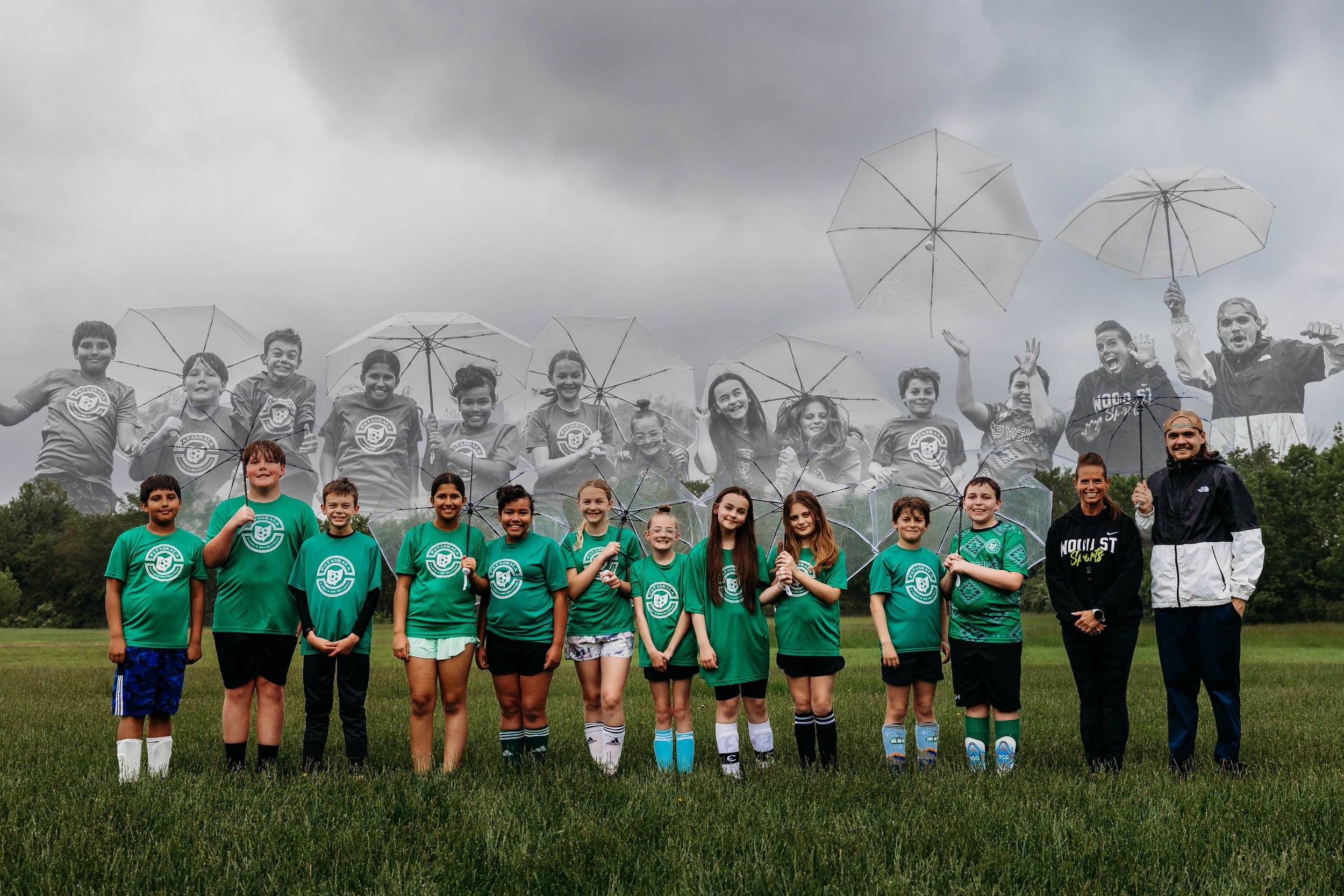 Youth soccer team in matching green jerseys poses outdoors on a grassy field under gray cloudy skies with umbrellas.