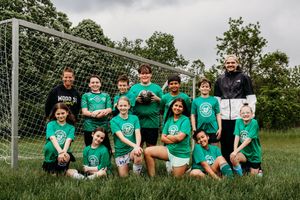 Youth soccer team in green jerseys poses together in front of a goal net on a grassy field.