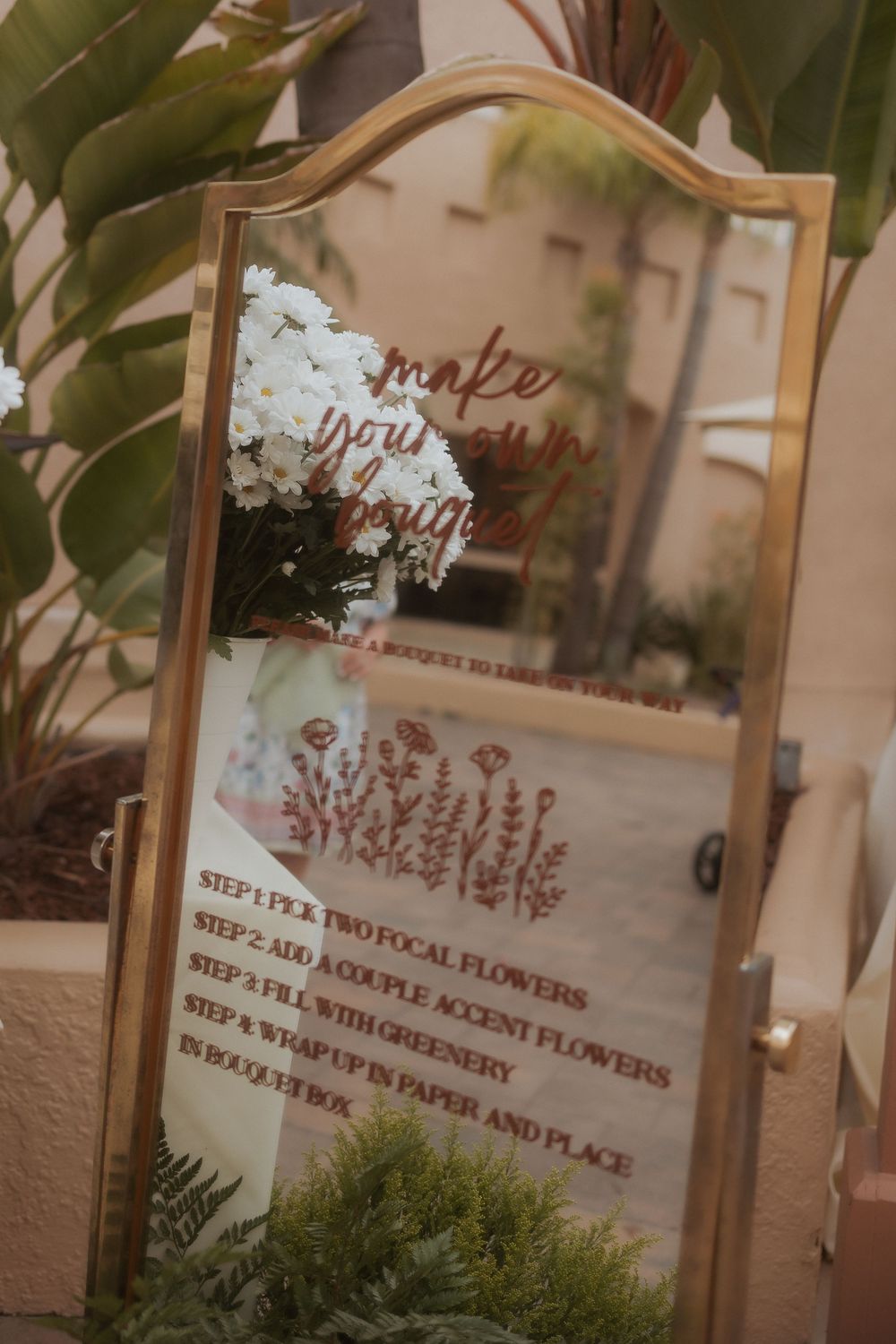 Decorative mirror with botanical flower arrangement instructions written in cursive and surrounded by green plants.