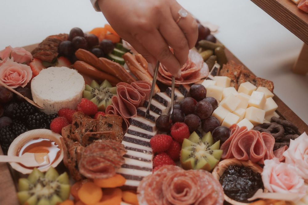 A beautifully arranged charcuterie board with meats, cheese, fruits and roses elegantly displayed.