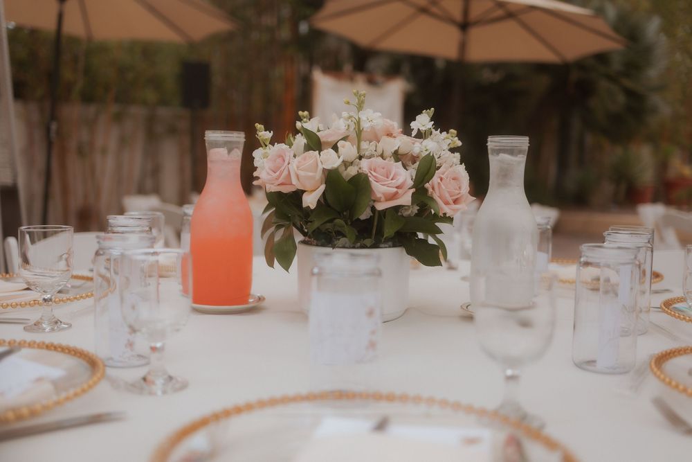 An elegant table setting with pink floral centerpiece, rose-colored cocktails, and gold-rimmed dishes at an outdoor reception.