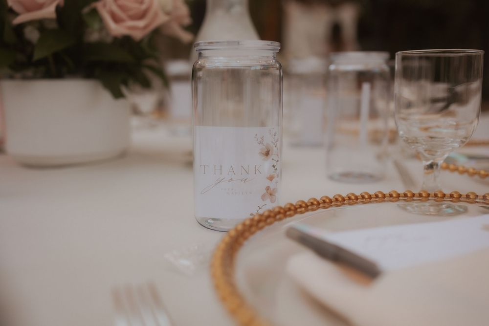 Close-up of an elegant place setting with a beer can styled cup and gold beaded charger plate on a white tablecloth.
