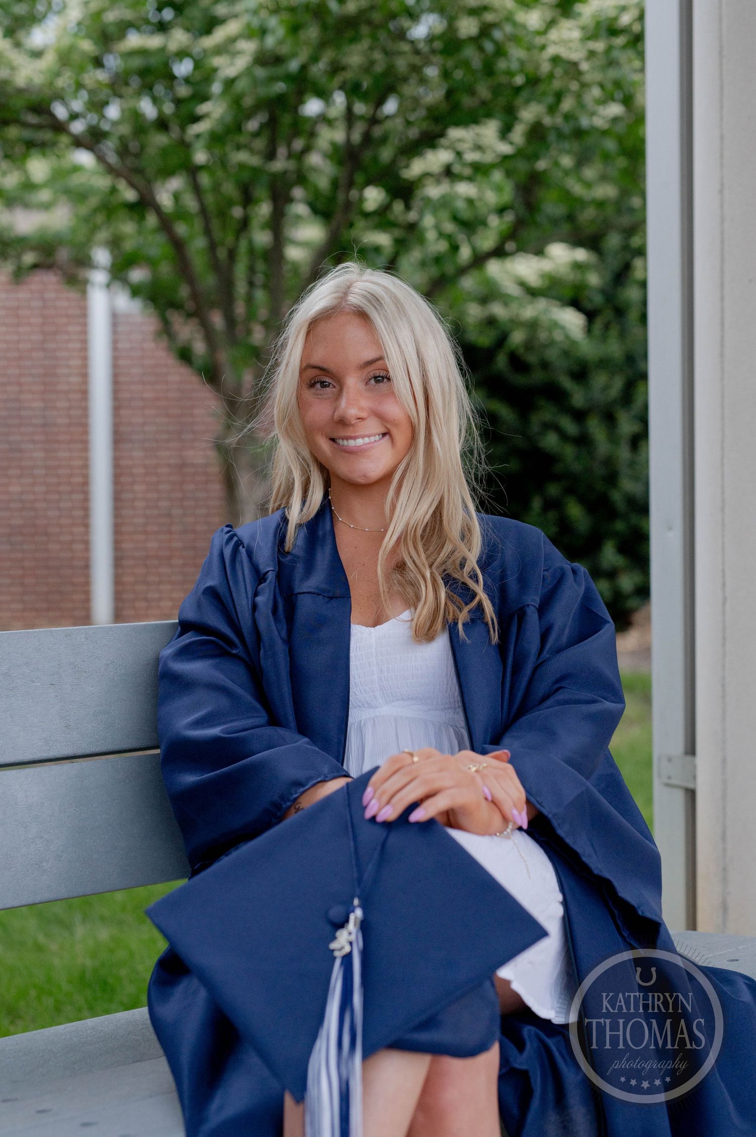 Three candid graduation photos show someone in a navy blue gown and blonde hair sitting outdoors by a brick building.