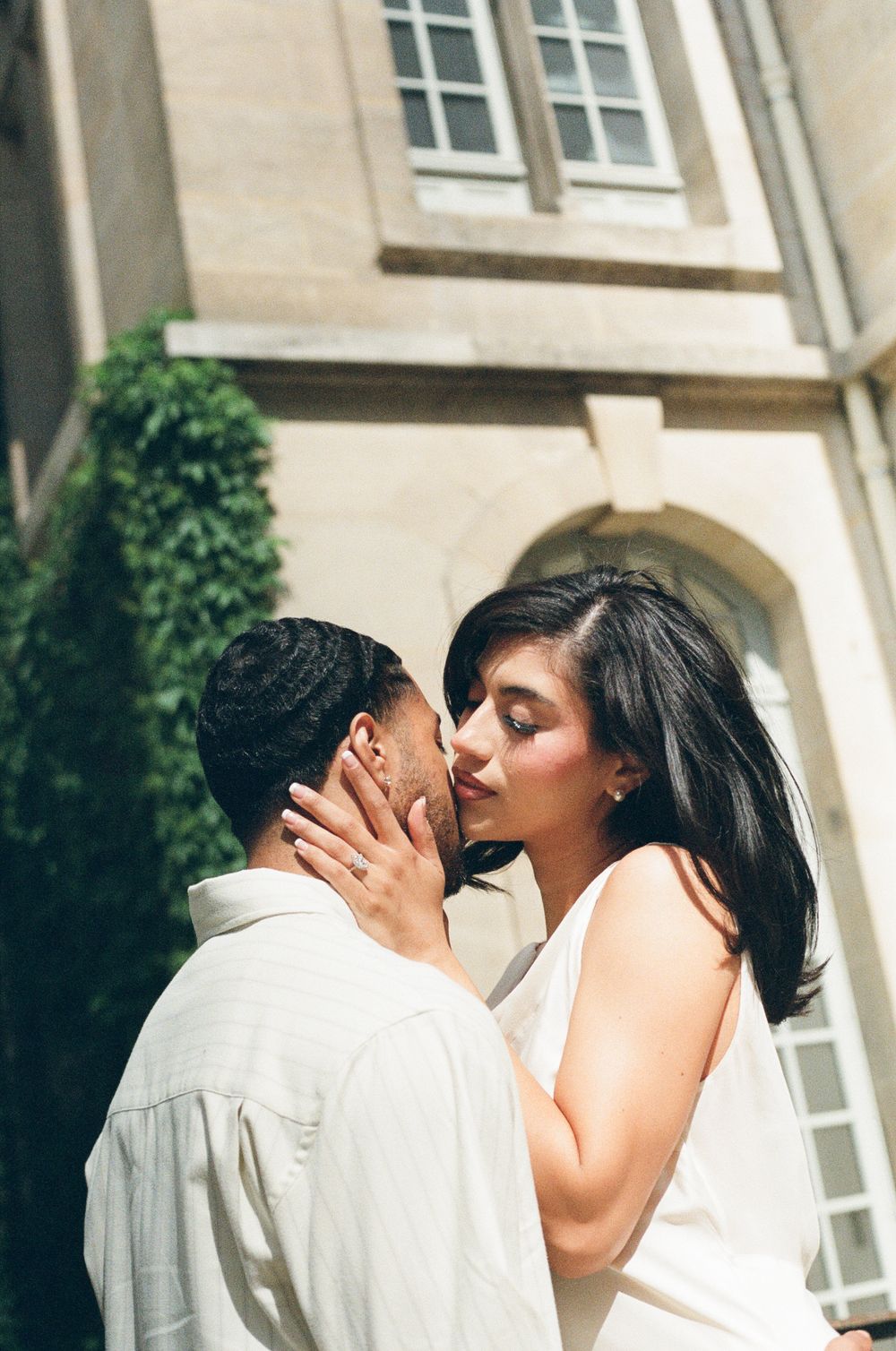 An intimate moment captured between a couple outside a classical building with stone architecture.